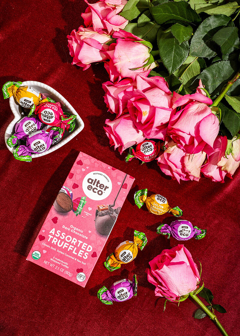 Assorted truffles in a heart-shaped dish with pink roses on a red background, featuring Alter Eco branding.